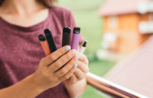 A woman holds different coloured vape pen products in her hand