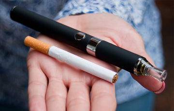 on the hand of a woman stands a pen vape and a twig of cigarettes